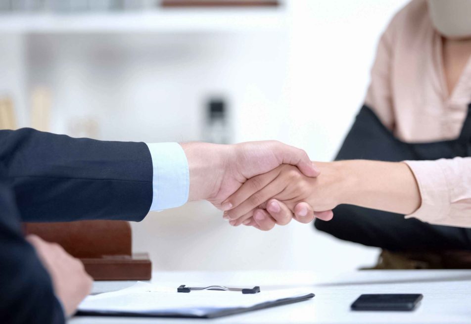 Two business people are shaking hands with papers in the table